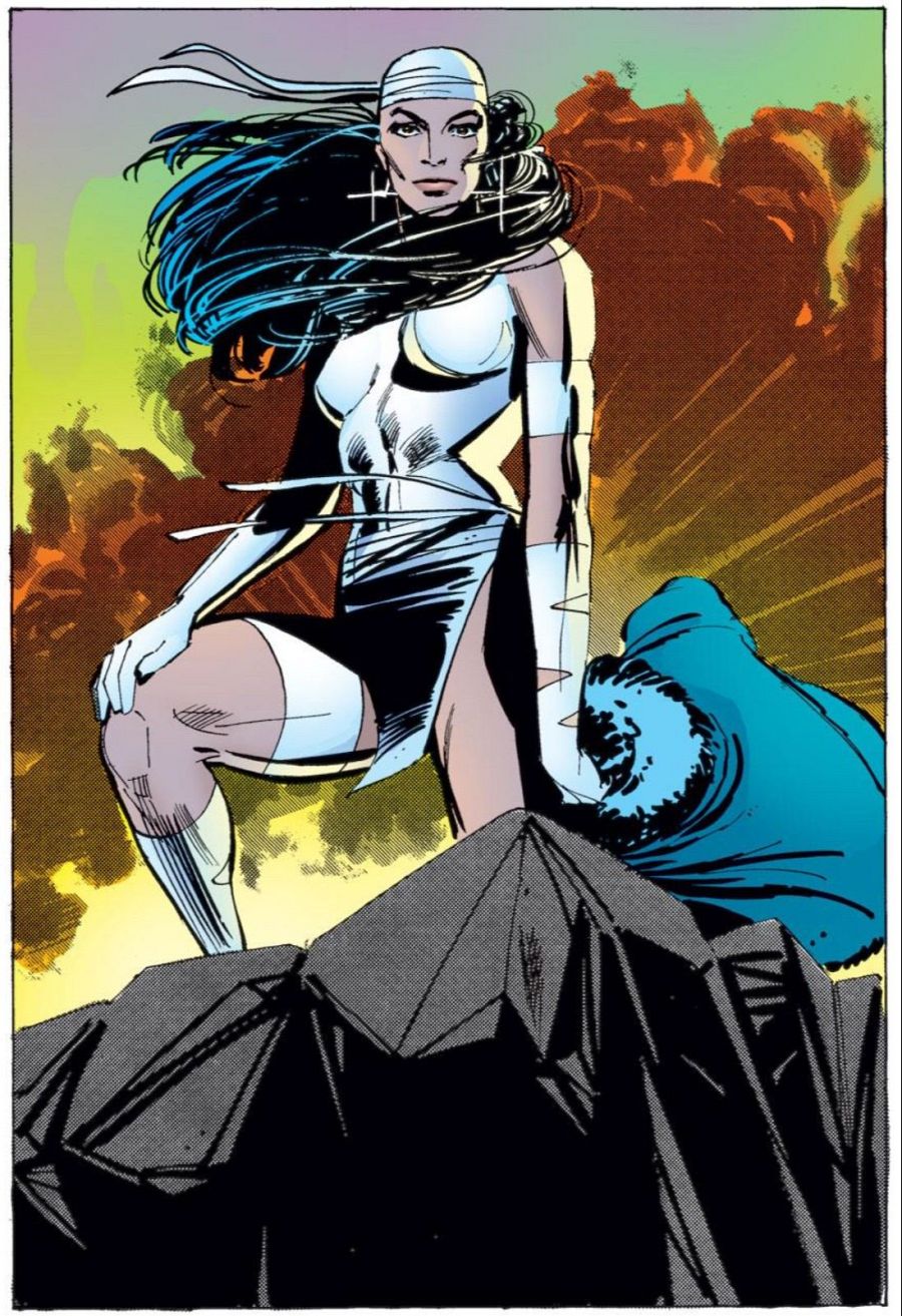 Elektra, en su traje blanco y negro, se yergue sobre rocas con una capa azul a sus pies, bajo un cielo anaranjado y amarillo.
