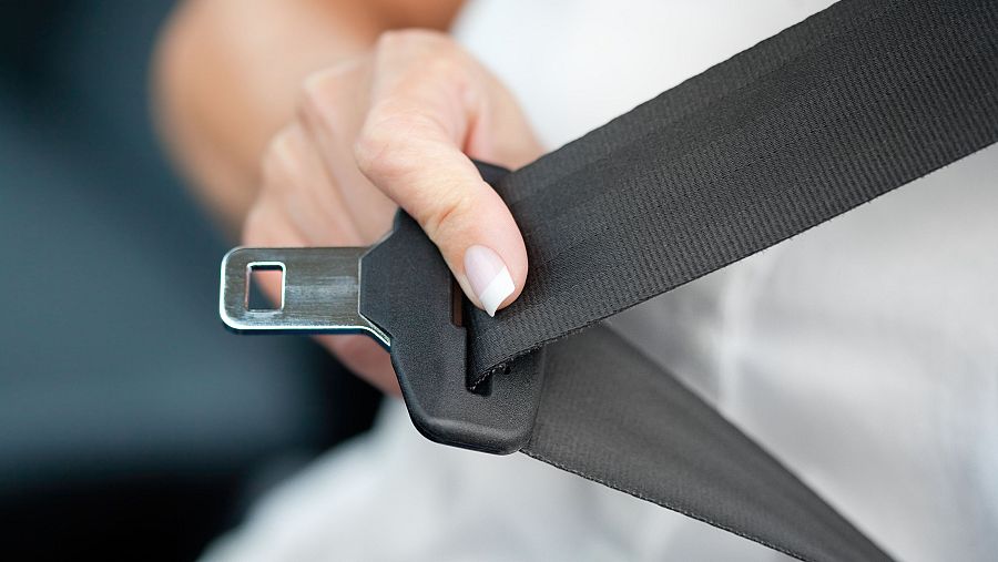 Mano tirando de la hebilla de un cinturón de seguridad para ajustarlo al cuerpo y evitar así accidentes graves de tráfico.