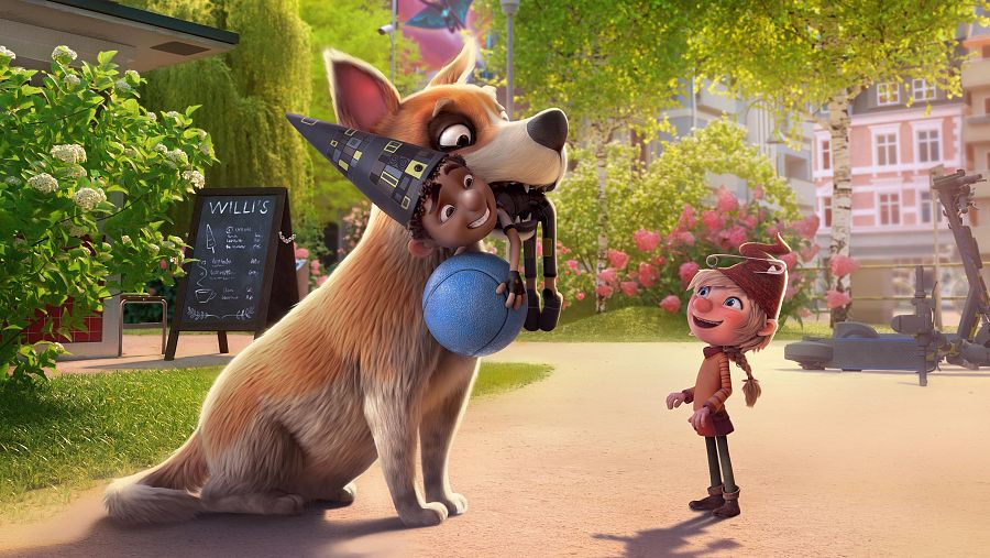 Perro sujetando a un niño sonriente con gorro de mago; un elfo observa cerca de un patinete y un puesto con una pizarra. Escena animada.