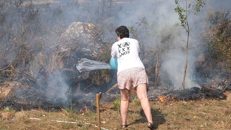 Una mujer intenta evitar que el fuego llegue a su casa este viernes, en Penagundín, en Melide (A Coruña).