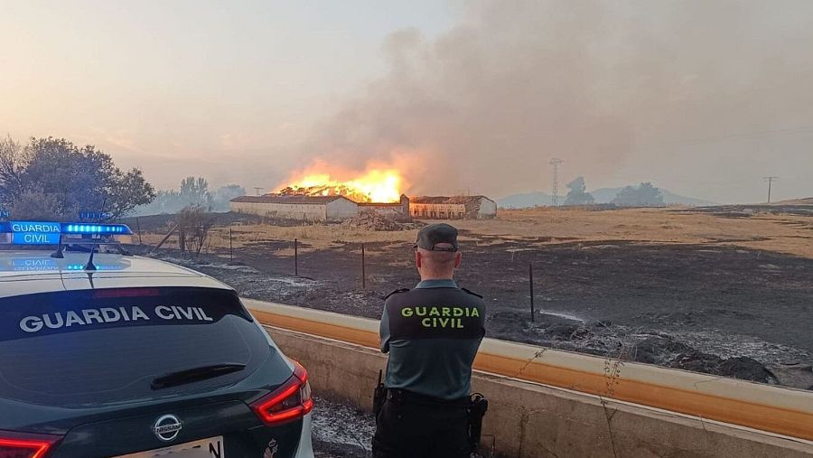 Un vehículo de la Guardia Civil junto a un efectivo del cuerpo en el incendio de Aldea del Cano (Cáceres)