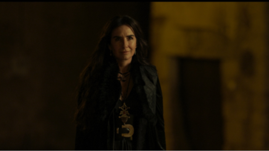 Maribel Verdú en primer plano, con expresión seria, mirando a cámara.  Atuendo oscuro, varios collares y fondo borroso con iluminación tenue.