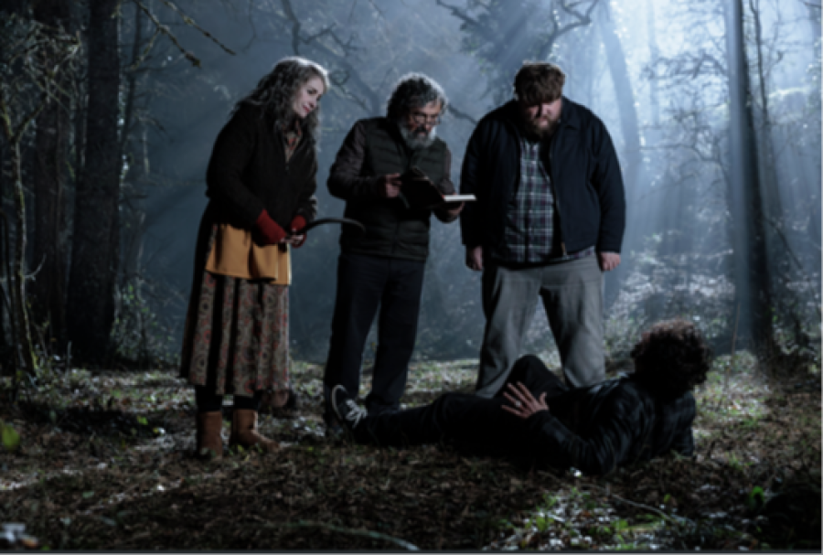 En un bosque oscuro, cuatro personas, una mujer con vara, un hombre leyendo y otros dos, uno en el suelo, generan una escena tensa en un fotograma de 'La coleccionista'.