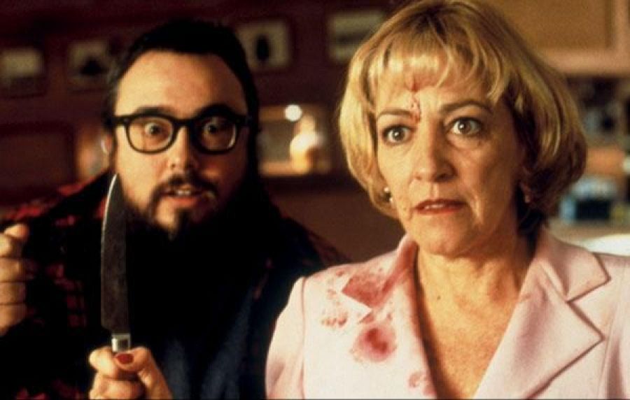 Escena de rodaje con Álex de la Iglesia (gafas, barba, cuchillo) y Carmen Maura (chaqueta rosa manchada), mostrando expresiones de miedo o sorpresa.