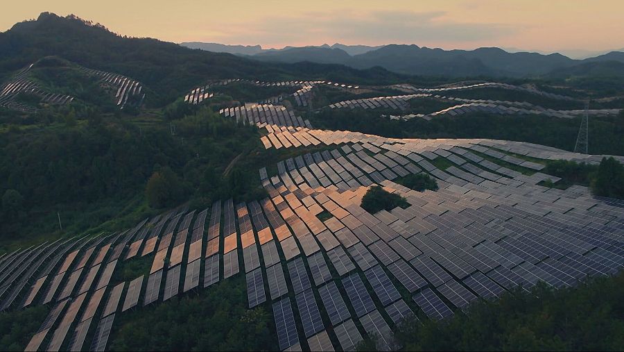 Panorámica aérea de paneles solares en un terreno montañoso, integrados en el paisaje natural.  Luz de atardecer.