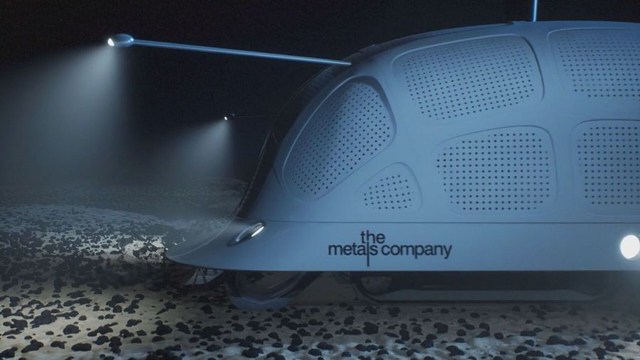 Vehículo submarino blanco grisáceo, con forma redondeada y dos focos, recolecta minerales del fondo marino rocoso.