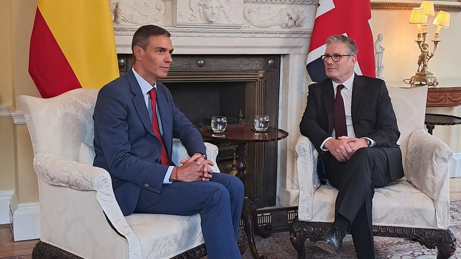 Encuentro entre dos líderes políticos en Downing Street.  Uno viste traje azul marino y corbata roja; el otro, traje oscuro y corbata granate.  Ambas banderas nacionales presentes.