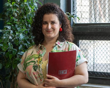Mujer con camisa floral y carpeta roja (EC3F) en interior.  Imagen publicitaria con texto 