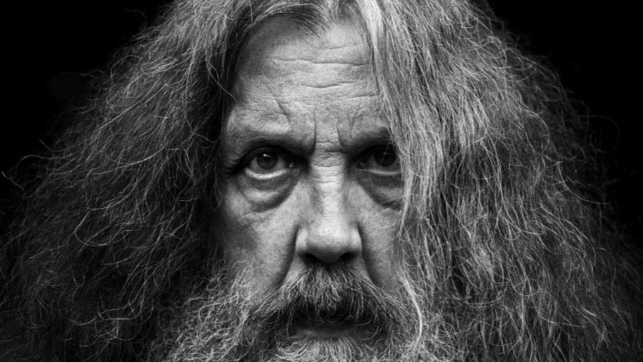 Retrato en blanco y negro de un hombre de cabello y barba largos, en primerísimo primer plano, mirada directa y fondo oscuro.