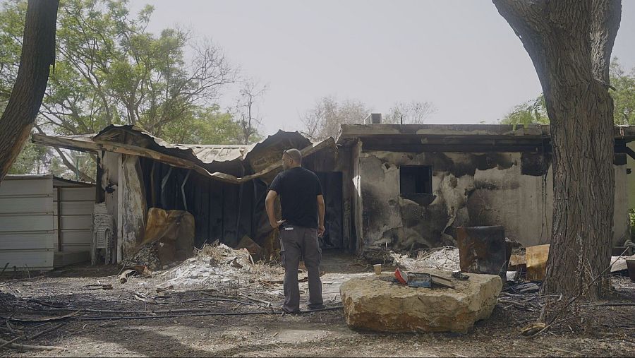 Hombre de pie ante una casa destruida por el fuego, con escombros y paredes ennegrecidas.  Se observa devastación y pérdida.