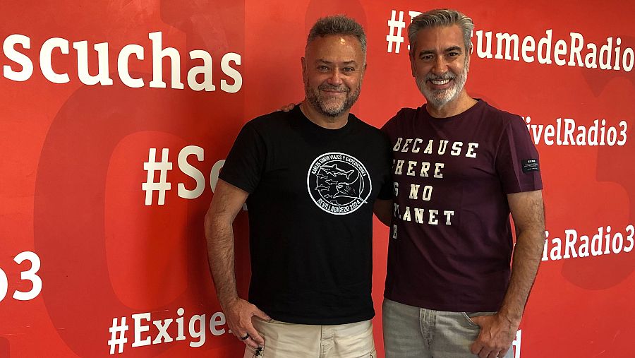 Dos hombres con camisetas con diseños distintos posan ante un panel rojo con el logo de Radio 3 y hashtags como #Escuchas, #SumedeRadio y #velRadio3.