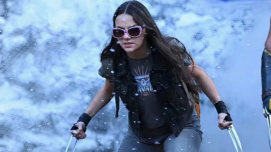Imagen de Daphne Keen con gafas rosas, chaleco y garras metálicas, en una escena borrosa de tonos claros, aparentemente en movimiento.