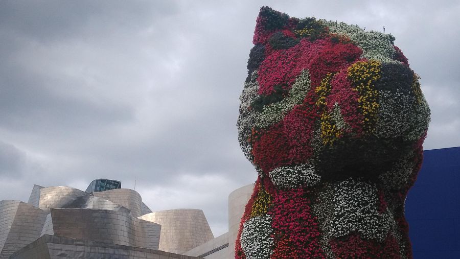Escultura floral 'Puppy' de Jeff Koons frente al Museo Guggenheim de Bilbao con su fachada metálica de fondo.