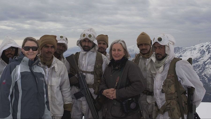 Mujeres con miembros de seguridad en uniforme blanco en paisaje nevado.  Uniformes con capuchas y gafas protectoras. Posible contexto periodístico.
