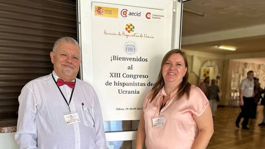 Oleksandr Pronkevich, presidente de la Asociación de Hispanistas de Ucrania, y una mujer posan juntos en un evento. Se observa un cartel con logos y texto relacionado con un congreso en Ucrania, con fecha de septiembre de 2025.