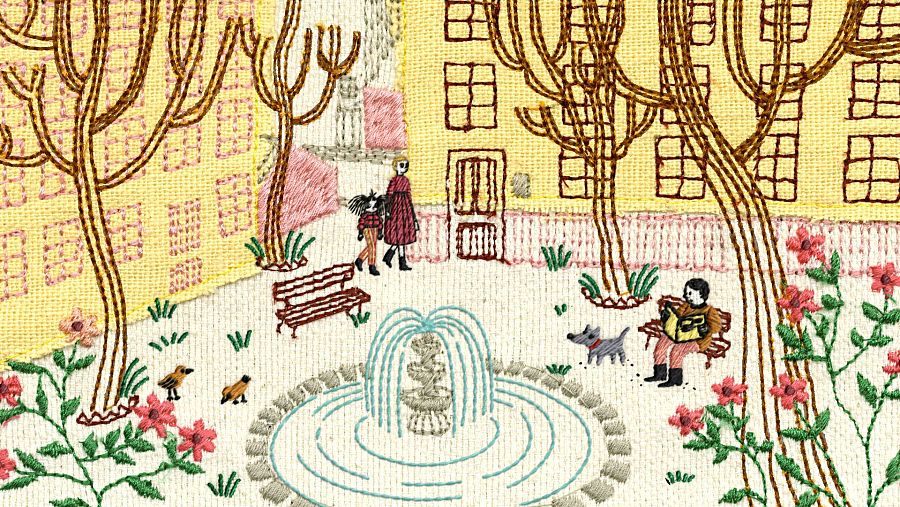 Un fotograma animado con estilo de bordado presenta una plaza con una fuente, edificios amarillos y árboles. Una mujer y una niña caminan, un hombre lee en un banco con un perro, y hay pájaros y flores.