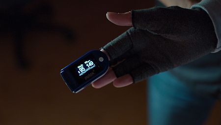 Un pulsioxímetro en el dedo de una persona con un guante sin dedos muestra una saturación de oxígeno del 95% y una frecuencia cardíaca de 149 latidos por minuto, un valor que podría indicar taquicardia.