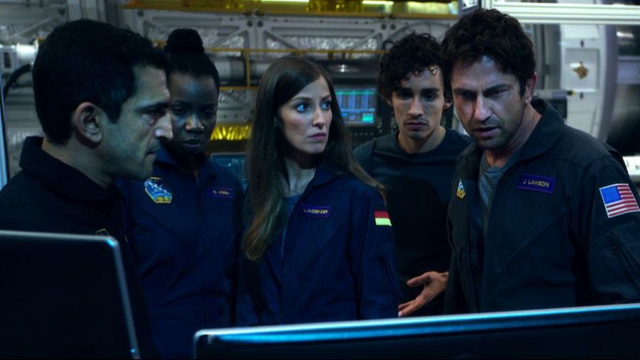 Un grupo de personas, posiblemente en una estación espacial, observa algo fuera de la imagen. Se distinguen varios individuos con uniformes, incluyendo a un hombre con una herida en la cara y otro con la bandera de Alemania en su uniforme.