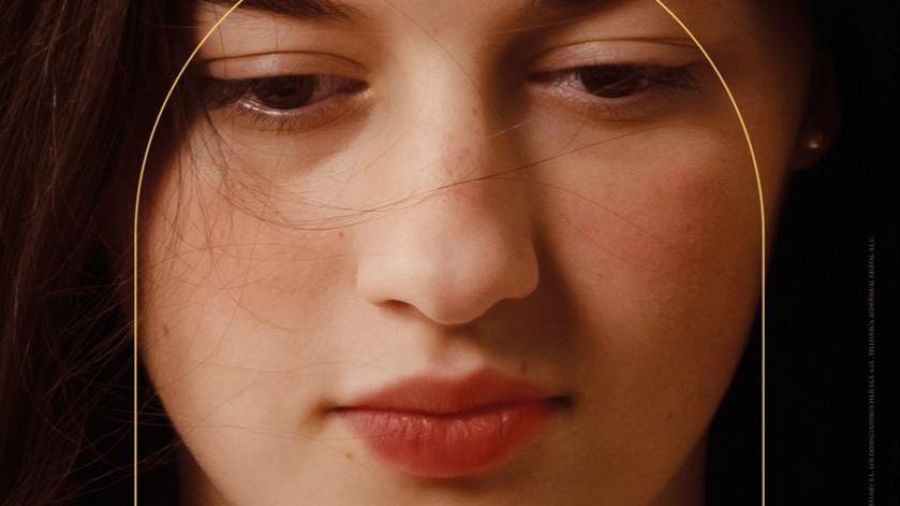 Primer plano de una joven con cabello oscuro y ojos marrones, mirando hacia abajo. Una línea dorada en forma de arco rodea su rostro. Sus labios son de color rosa pálido.