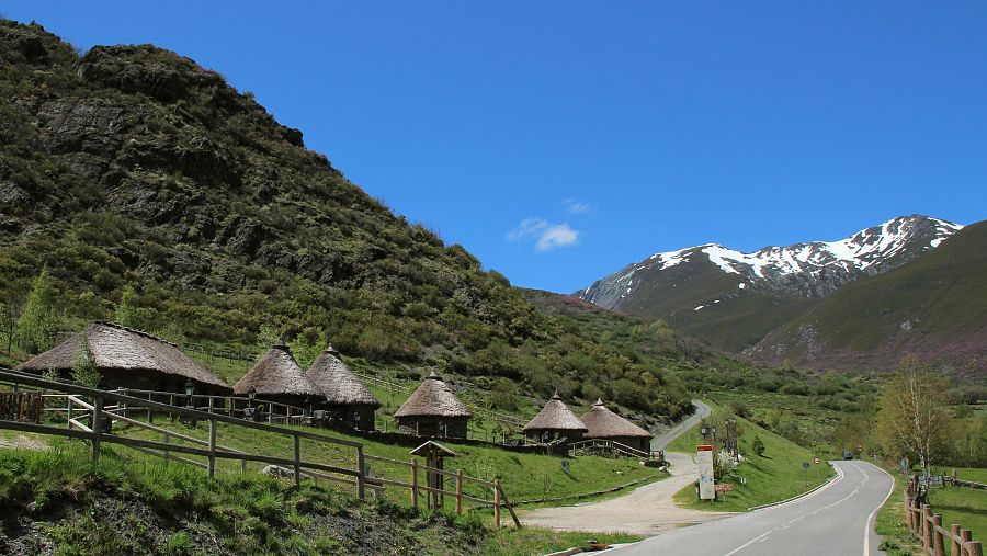 Centro de Interpretación del Castro de Chano con varias pallozas tradicionales y montañas nevadas al fondo en el valle de Laciana, León.