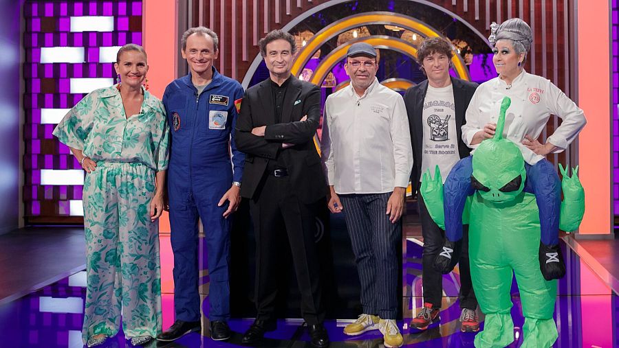 Un grupo diverso posa en un estudio televisivo; se observa a un hombre con traje negro, otro con camisa y gorra, y una mujer con un conjunto estampado. Destacan un astronauta y una persona disfrazada de extraterrestre.