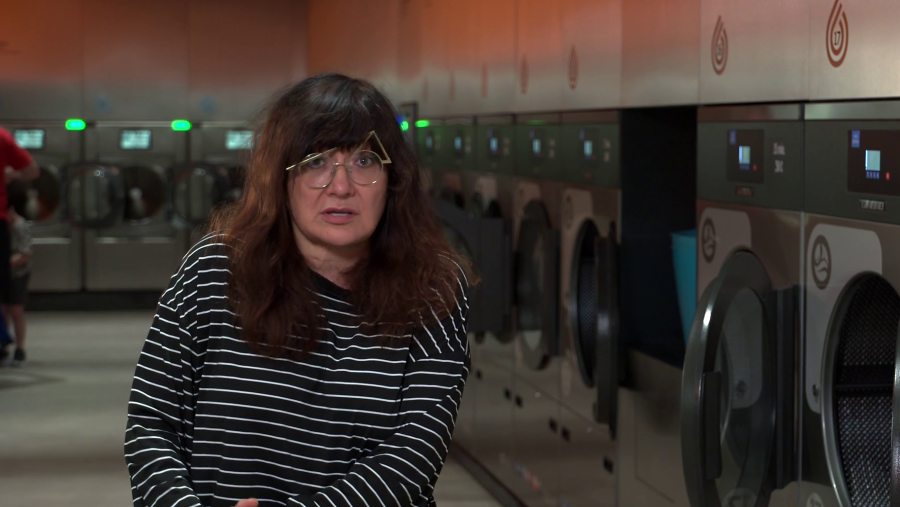 Isabel Coixet, con gafas de montura dorada y camiseta a rayas, posa en una lavandería frente a varias lavadoras industriales.