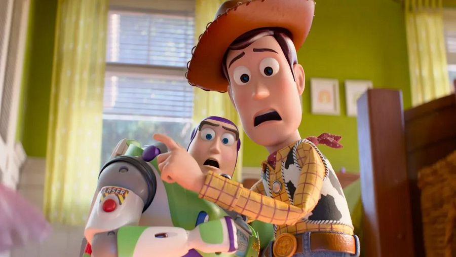 En un fotograma de la película, dos personajes icónicos reaccionan con sorpresa. Uno, vestido con atuendo de vaquero, señala algo fuera de la imagen, mientras que el otro, con un traje espacial, comparte su asombro.