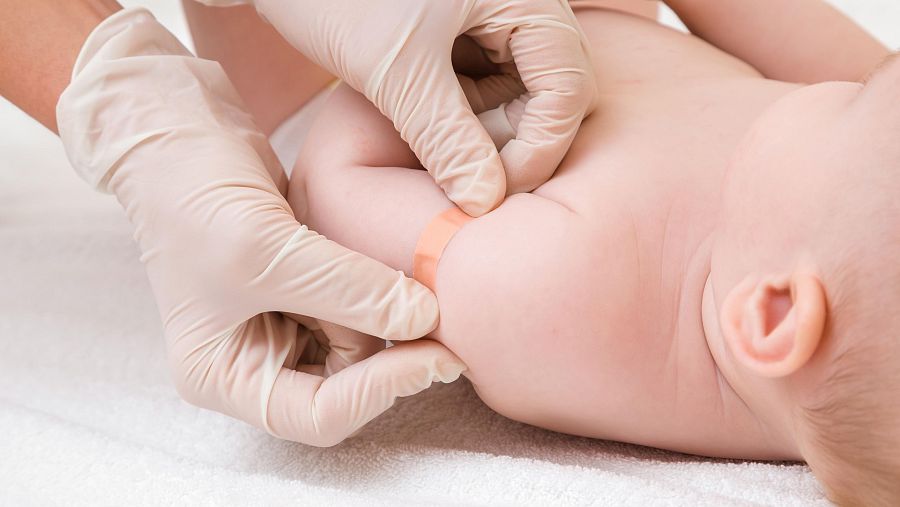 Las manos de un sanitario colocan una tirita en un niño tras vacunarle de hepatitis B