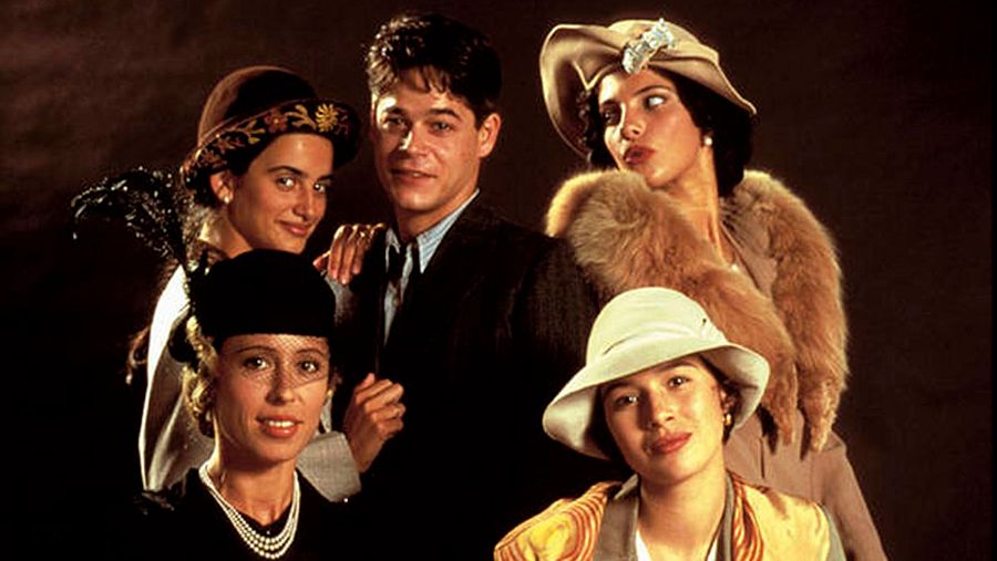 Un grupo de cinco personas posa elegantemente, evocando la Belle Époque. El hombre viste un traje oscuro y las mujeres llevan sombreros adornados y abrigos, creando una atmósfera de sofisticación.