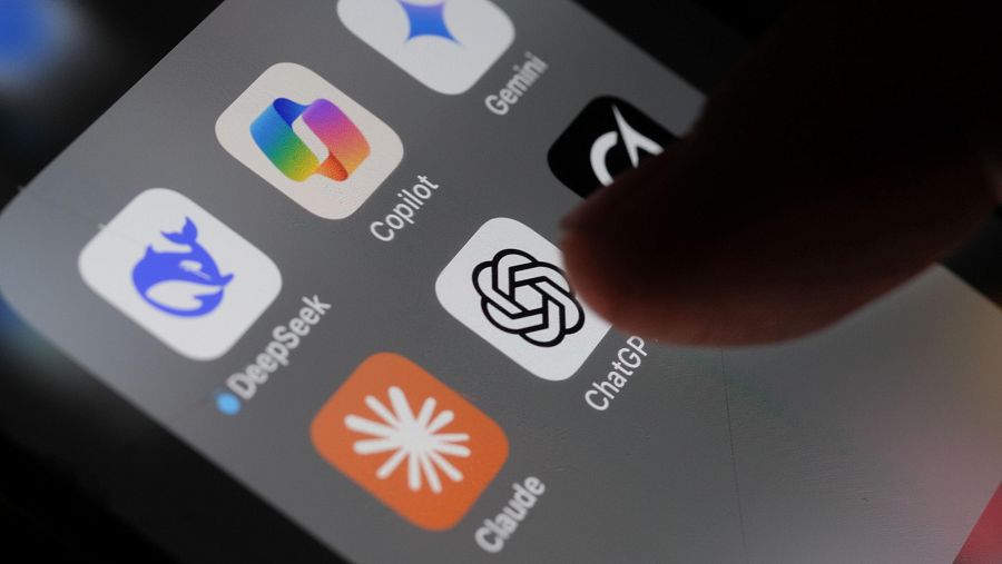 La pantalla de un teléfono móvil muestra diversas aplicaciones, incluyendo iconos de herramientas de IA como ChatGPT, Copilot, Gemini, DeepSeek y Claude. Un dedo interactúa con la pantalla, seleccionando una de las aplicaciones.