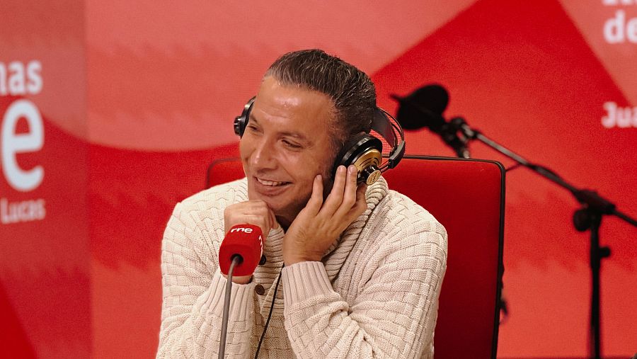 Pitingo, en un estudio de radio, con auriculares y un jersey crema, frente a un micrófono rojo con el logo de RNE.