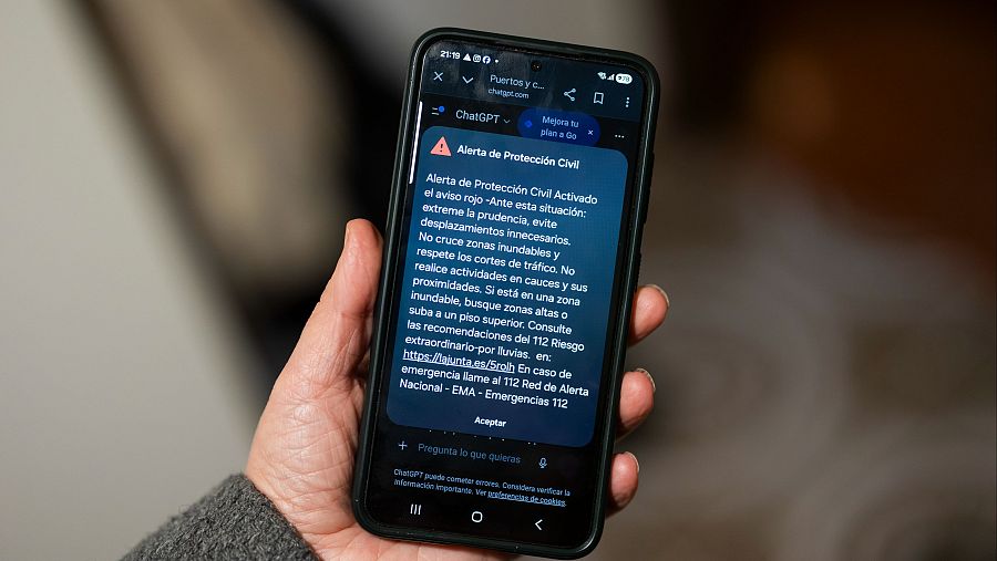 Una persona sostiene un teléfono móvil con la alerta enviada por protección civil de aviso rojo