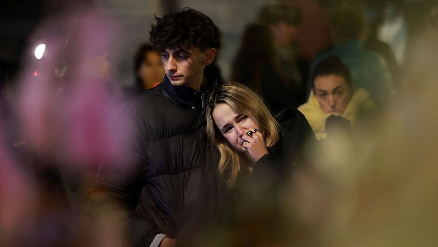 Una pareja de jóvenes, consternados, ante el altar de flores y velas creado en homenaje a las víctimas del incendio