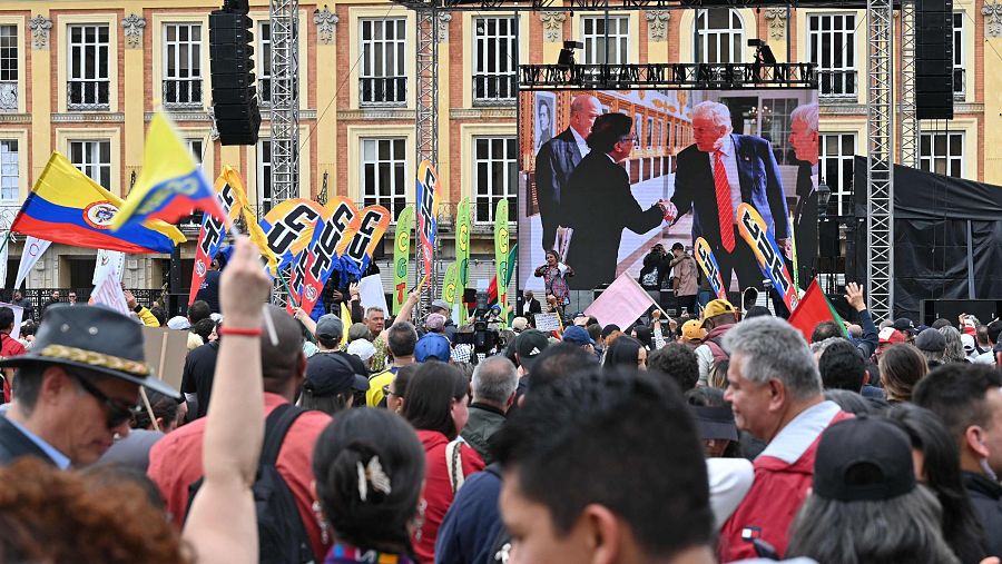 En Bogotá, una multitud observa una pantalla que muestra a Donald Trump y Gustavo Petro. Los asistentes, ondeando banderas, se encuentran frente a un edificio, capturando un momento de la reunión entre ambos líderes.