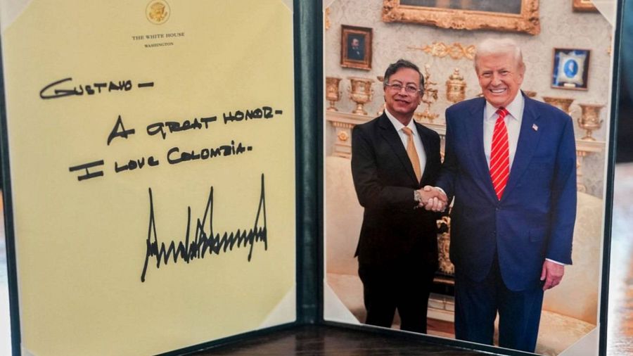 En la imagen, dos hombres en trajes formales se dan la mano. Uno de ellos, con corbata a rayas, sostiene una nota manuscrita. El otro, con corbata dorada, parece estar en un encuentro oficial.