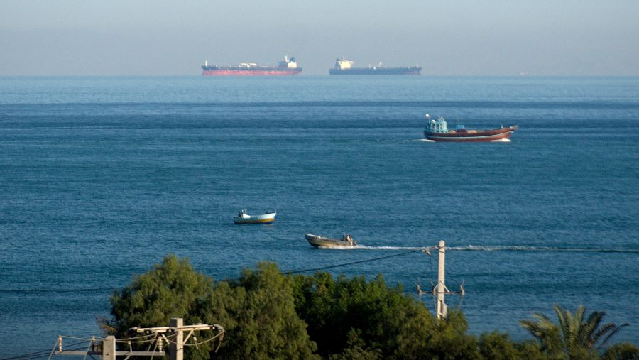 Una escena marítima en el Estrecho, con vegetación costera y diversos barcos navegando. Se distinguen barcos de carga, un pesquero y pequeñas embarcaciones, con el mar en calma y un cielo despejado.