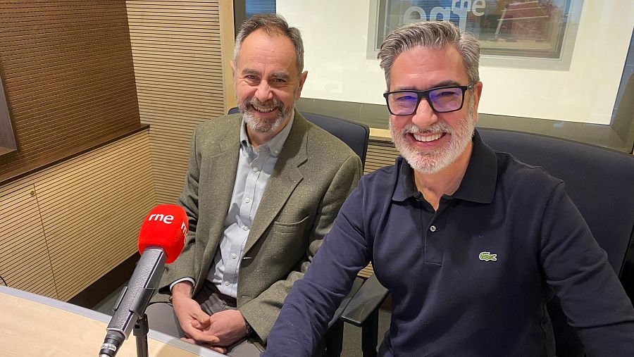Dos hombres, Ricardo Martino y Arturo Martín, posan sonrientes en un estudio de radio frente a un micrófono con el logo de RNE, con paneles de madera en el fondo y el logo de RTVE en la pared.