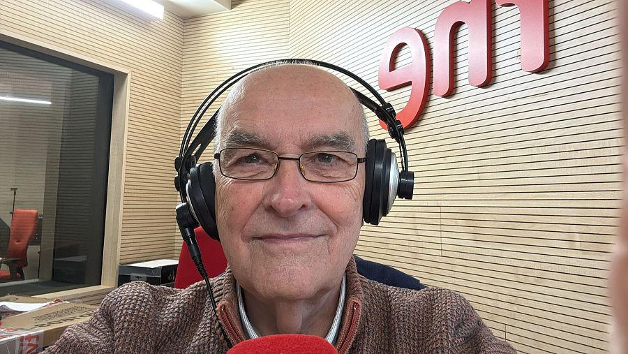 Enric Benito, con gafas y auriculares, sonríe a la cámara en lo que parece ser un estudio de radio, con el logo de una emisora en el fondo.