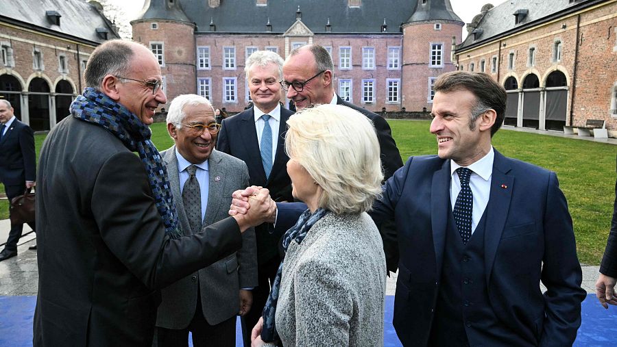 Un grupo de personas, entre ellas figuras políticas, se encuentran reunidas frente a un edificio. Se observa un saludo entre dos personas, mientras que otras, como Emmanuel Macron y António Costa, observan la escena.