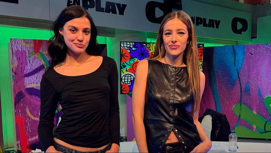Dos mujeres jóvenes se encuentran en un estudio de televisión. Una lleva una camiseta negra y un collar dorado, y la otra un chaleco de cuero negro. El fondo presenta grafitis coloridos y el logo del programa.