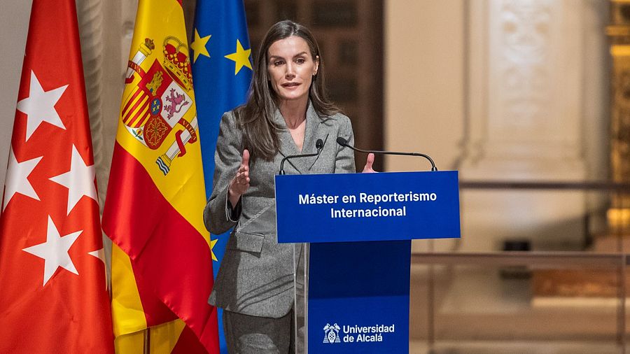 Una mujer, vestida con un traje gris, se encuentra frente a un atril. Detrás de ella, se ven tres banderas. El atril muestra un texto y un logo.
