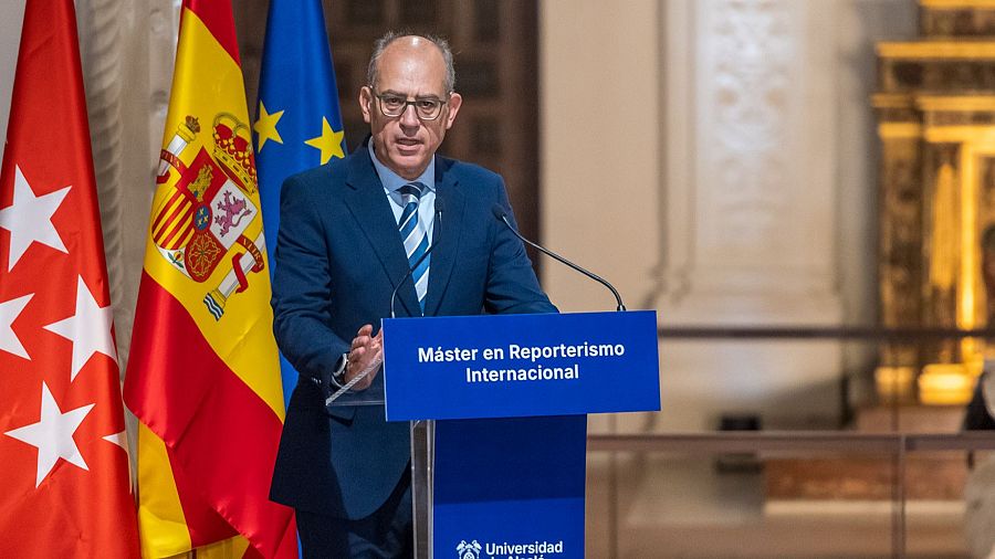 Un hombre con gafas y traje azul, posiblemente José Antonio Guardiola, se encuentra frente a un atril con el texto 