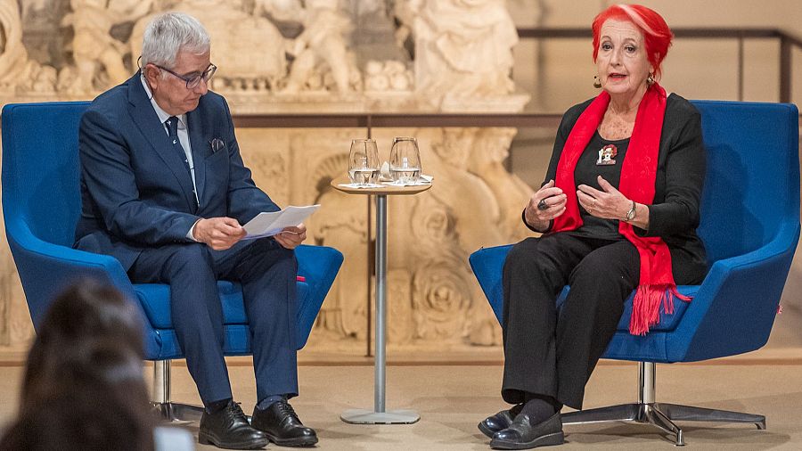 Dos periodistas, Alfonso Armada y Rosa María Calaf, se encuentran sentados frente a una mesa. Uno de ellos lee documentos, mientras que la otra persona, con vestimenta oscura y una bufanda, observa.