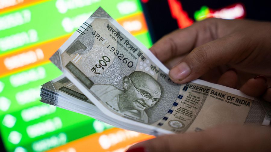 Una mano sostiene un fajo de billetes con la imagen de una figura y texto. Se distingue el número de serie de uno de los billetes.