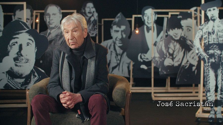 José Sacristán, con vestimenta oscura y bufanda gris, posa sentado con las manos entrelazadas. El fondo muestra imágenes en blanco y negro sobre una estructura de madera.