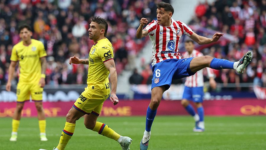 Nahuel Molina, del Atlético de Madrid, con la camiseta número 6, golpea el balón con el pie derecho, mientras un jugador rival observa la acción en un campo de fútbol.
