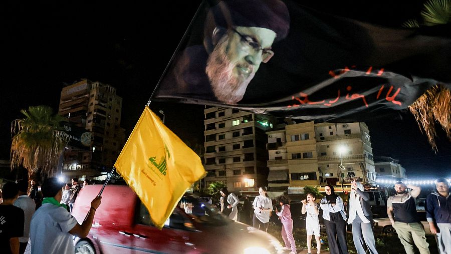 Un hombre sostiene una bandera con la imagen de Hassan Nasrallah mientras desplazados regresan a sus hogares en Líbano