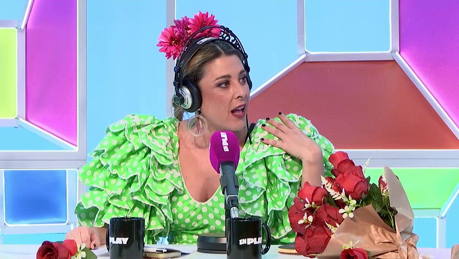 Cristina Pedroche, con vestido verde lima, flores fucsias y auriculares, posa en un estudio con un micrófono morado y tazas que muestran 