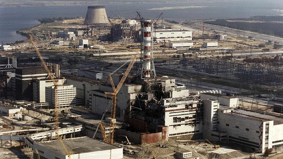 Vista aérea de la planta nuclear de Chernóbil el 1 de octubre de 1986, mostrando el Reactor 4 dañado, grúas y estructuras de reparación, con una torre cilíndrica roja y blanca y una torre de refrigeración al fondo.