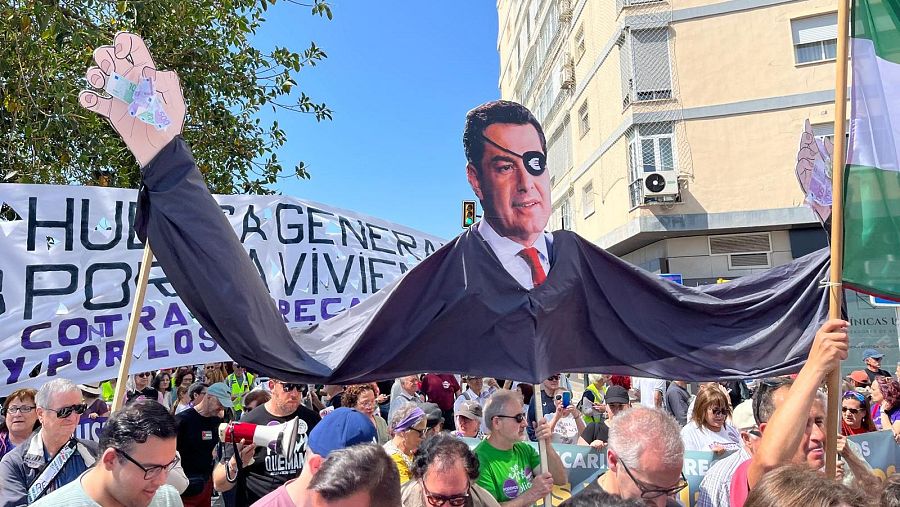 Manifestantes portan en Málaga una pancarta con una caricatura del candidato del PP a la reelección, Juanma Moreno.